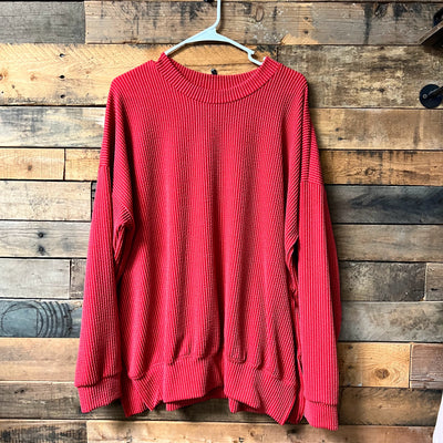 Red ribbed sweater on a hanger against a wooden wall.