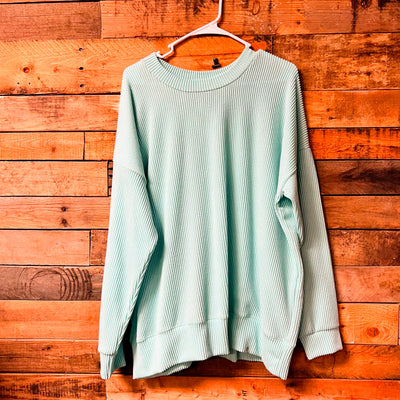 Light green sweater on a hanger against a wooden wall