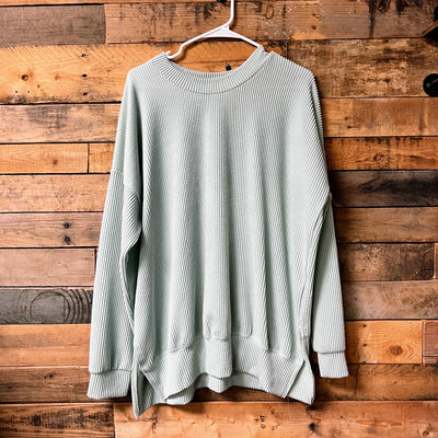 sage sweater on a hanger against a wooden wall