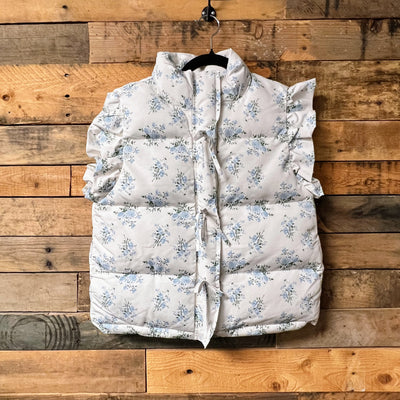 Floral-patterned puffer vest on a hanger against a wooden background