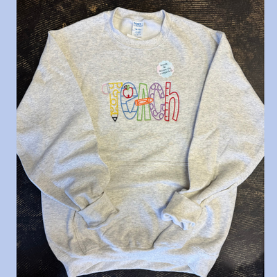 Gray sweatshirt with colorful 'Teach' text on a dark surface